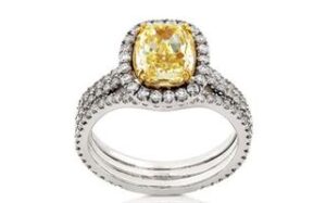 A dazzling ring features a large cushion-cut yellow diamond at its center, surrounded by a halo of smaller white diamonds set in a white gold band that is also encrusted with white diamonds, adding to its sparkle and elegance.