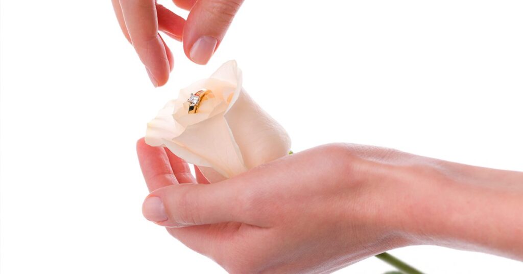 A woman plucks an engagement ring from the center of a delicate white rose