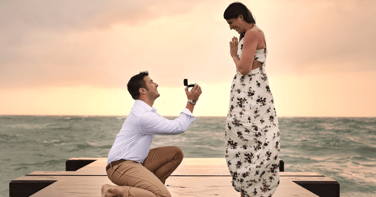 A man proposes to his girlfriend at sunset in front of the ocean with the perfect engagement ring style for her