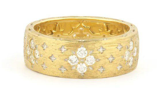 The Jude Frances Moroccan Wide Band With Flower Diamond Pattern features a gold ring embellished with diamond clusters arranged in elegant floral patterns and set against a textured band background with additional small diamond accents, creating an intricate and luxurious design.