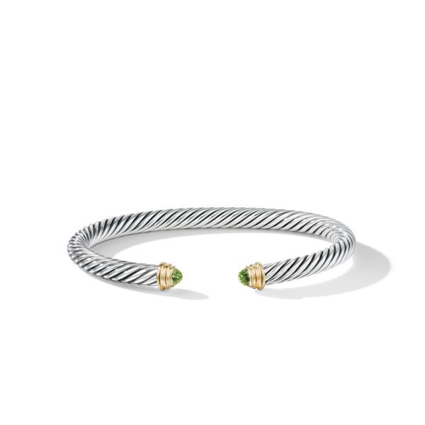 A twisted silver bracelet with open ends, featuring green gemstones encased in gold settings at each tip, displayed on a plain white background.