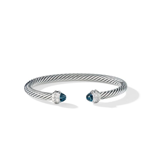 A twisted silver cuff bracelet with open ends, each adorned with a round, blue gemstone set in a silver bezel and surrounded by small, clear crystals. The bracelet is minimalist and elegant, displayed on a white background.