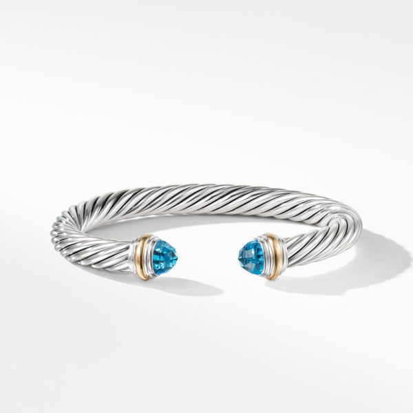 A sleek, twisted silver cuff bracelet with open ends, featuring polished blue gemstone caps encased in gold accents. The bracelet has a modern, elegant design and is set against a clean, white background.