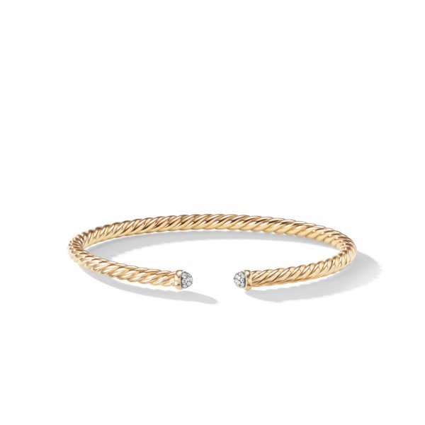 A sleek and elegant bracelet made of twisted gold. The open-ended bangle features two round, silver embellishments with diamond-like stones at each end, creating a sophisticated and luxurious look. The bracelet is set against a plain white background.