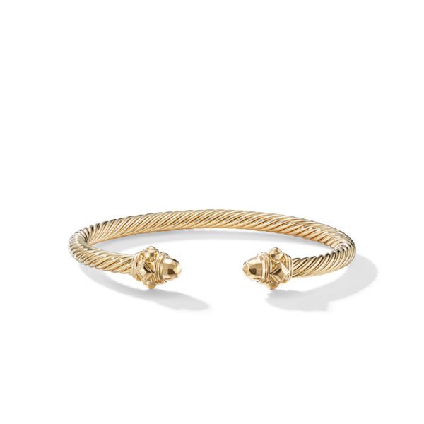 A gold cuff bracelet with a twisted rope design. The open ends of the bracelet are capped with ornate details featuring a polished gold finish, adding a touch of elegance and sophistication. The bracelet casts a slight shadow on a white background.