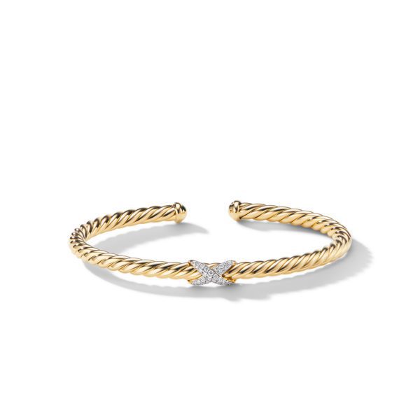 A gold twisted cable bracelet featuring a decorative X-shaped centerpiece adorned with small, sparkling gemstones. The bracelet is open-ended, showcasing an elegant and timeless design with a luxurious appeal.