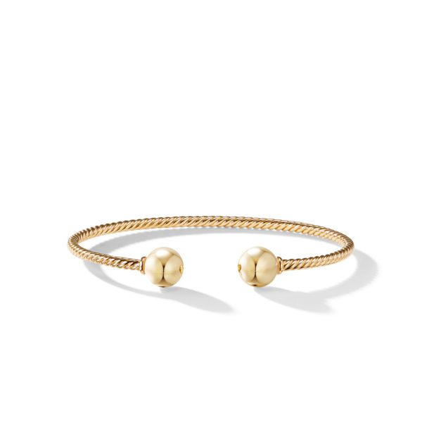 A gold cuff bracelet featuring a twisted design with polished spheres at both open ends, resting on a white background.