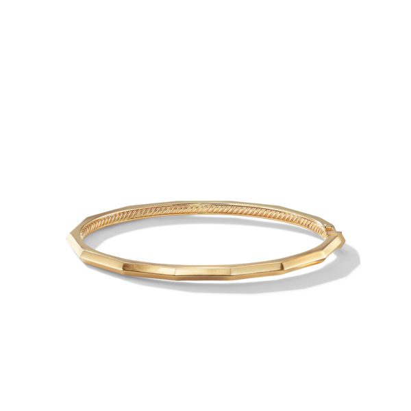 A close-up image of a thin, gold bangle bracelet with a slightly angular, geometric shape. The bracelet has a smooth finish and a subtle, understated design, displayed against a plain white background.