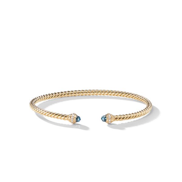 A twisted gold cuff bracelet with open ends is adorned with blue gemstone caps, accentuated by small diamonds. The bracelet is displayed on a plain white background.