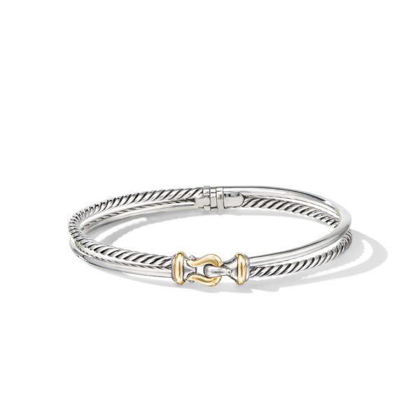 A silver and gold bangle bracelet with a twisted design and a clasp featuring a distinctive gold accent. The bracelet has a mix of smooth and textured surfaces, adding a stylish, elegant look. The background is plain white.