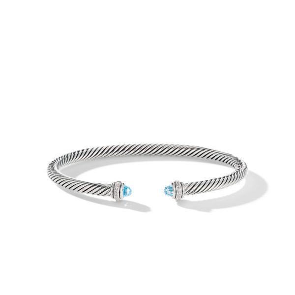 A silver twisted cable cuff bracelet featuring blue gemstone end caps mounted in silver settings. The cuff is open-ended with intricate detailing around the blue stones. The bracelet is displayed on a white background.