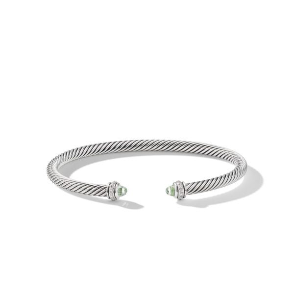 A silver twisted cable cuff bracelet with open ends, each adorned with a small, round green gemstone and an intricate silver design surrounding the stones. The bracelet is displayed against a plain white background.