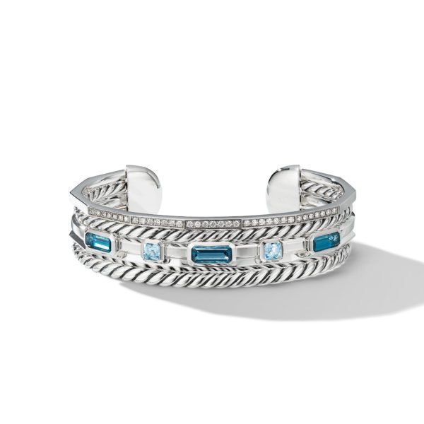 A silver cuff bracelet featuring a twisted rope design, adorned with alternating blue and clear rectangular gemstones and a row of small clear stones along the top edge. The bracelet is open-ended with intricate detailing, casting a shadow on a white background.