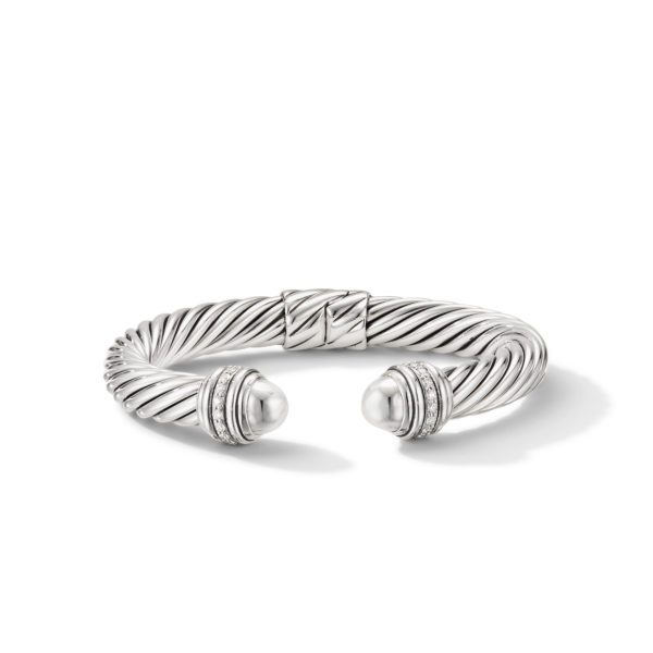 A silver cuff bracelet with a twisted rope design and open ends. Each end is capped with a pearl-like bead surrounded by small, sparkling stones. The bracelet has a sleek and elegant appearance, casting a soft shadow on the white surface beneath it.