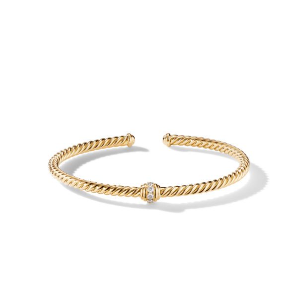 A twisted gold cuff bracelet with a sleek design, featuring a small, central band adorned with tiny, sparkling diamonds. The bracelet is open-ended and rests on a plain white background, casting a delicate shadow.