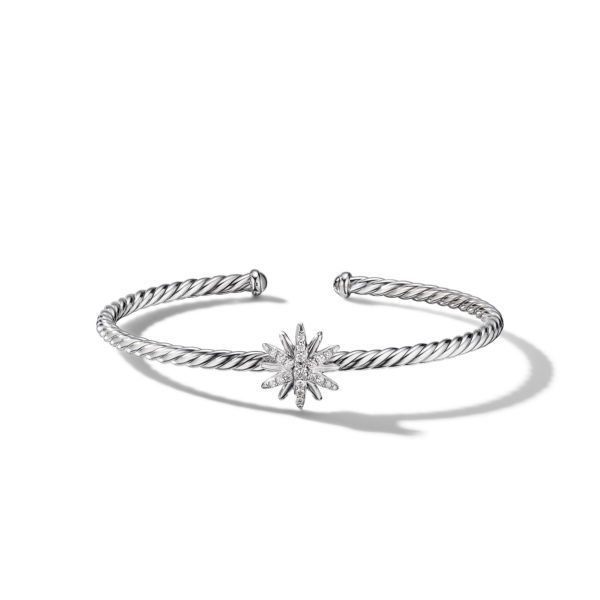 A silver cuff bracelet with a twisted rope design ends in an open circle. At the center, it features a starburst motif adorned with small crystals or diamonds, adding a touch of sparkle. The bracelet casts a soft shadow on a plain white background.