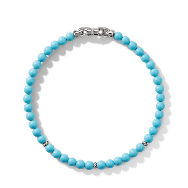 A turquoise bead bracelet with a silver clasp is arranged in a circular shape. Small silver accent beads are interspersed among the turquoise beads, adding subtle detailing. The bracelet has a bright and polished appearance.