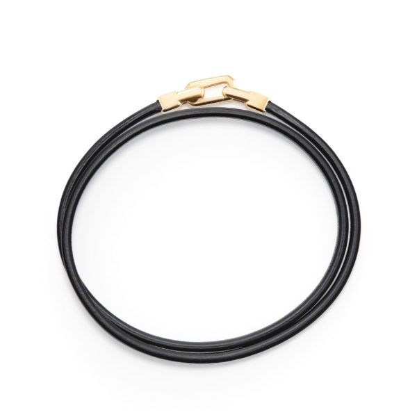 A double black leather bracelet features a sleek design with gold-tone clasps, creating a stylish and contemporary accessory. The bracelet is coiled into a circular shape, highlighting its simplicity and elegance.