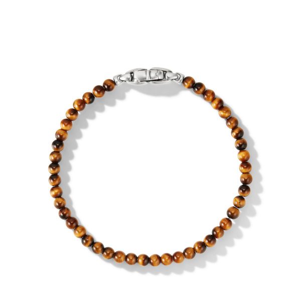 A bracelet made of polished brown tiger's eye beads, fastened with a sleek silver clasp, is arranged in a circular shape on a plain white background. The beads display varying shades of brown, creating a visually appealing pattern.