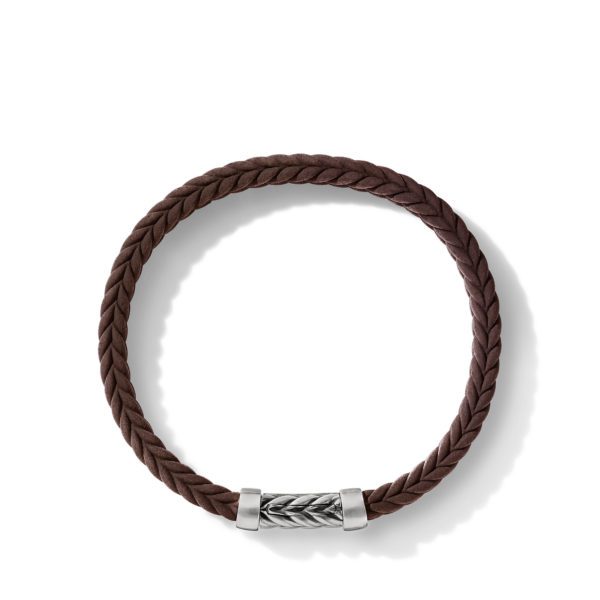 A brown braided leather bracelet with a silver clasp featuring an intricate woven design. The bracelet is set against a plain white background, casting a soft shadow beneath it.