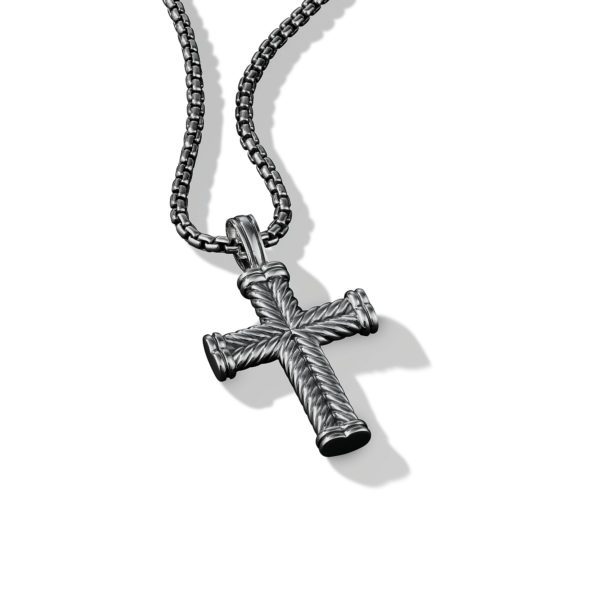 A close-up image of a silver cross pendant with a rope-like texture, hanging from a matching silver chain. The pendant is centrally placed against a white background, exhibiting subtle shadows that highlight its detailed and intricate design.