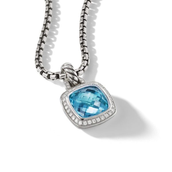 A silver box chain necklace featuring a pendant with a square-cut blue gemstone surrounded by a border of small clear crystals, set in a silver frame. The pendant catches the light, highlighting the facets of the gemstone and the shine of the silver.