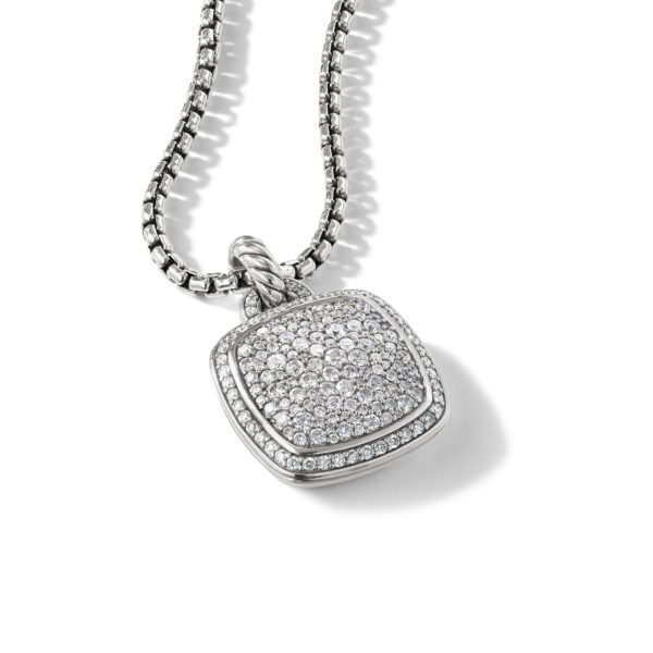 A delicate silver necklace with a square pendant encrusted with small, sparkling diamonds. The pendant has a slightly rounded shape and hangs from a chain featuring uniform, rectangular links. The background is white, highlighting the jewelry's brilliance.