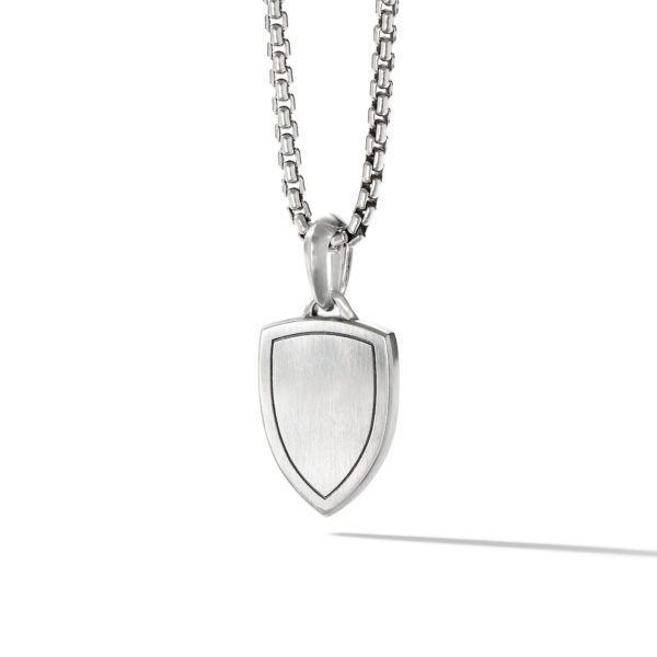 A silver necklace featuring a shield-shaped pendant with minimal detailing. The chain has a box link design and the pendant has a smooth, polished surface. The necklace is displayed against a white background.