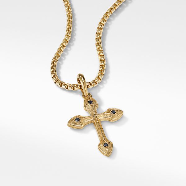 A gold chain with a gold cross pendant. The pendant features intricate detailing and four small black gemstones, one at each end of the cross. The chain has a textured design and the overall appearance is elegant and sophisticated, set against a white background.