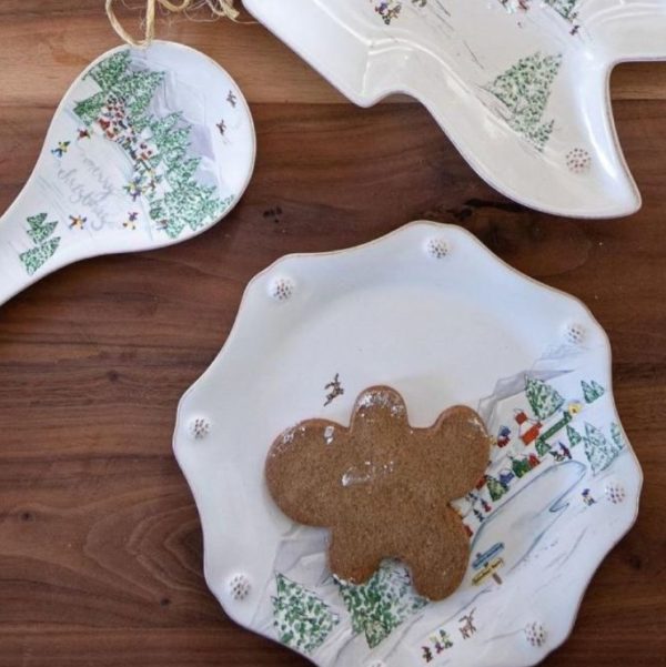 An overhead view reveals a festive holiday-themed table setting, featuring the Juliska Berry & Thread Dessert/Salad Plate - North Pole adorned with a charming gingerbread man cookie. The table also showcases a matching spoon rest and another dish, all beautifully designed with similar wintery motifs on the wooden tabletop.