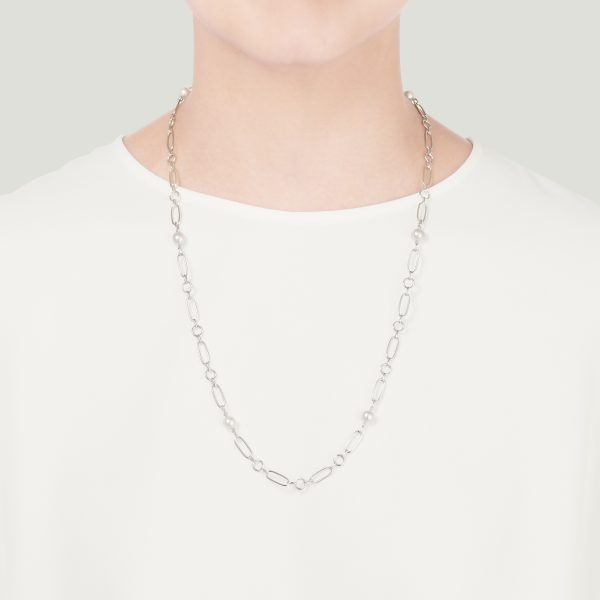 A person wearing a simple white shirt is adorned with a delicate Mikimoto 6.5mm Akoya Cultured Pearl Necklace. The background is plain and light-colored, placing emphasis on the elegant jewelry.