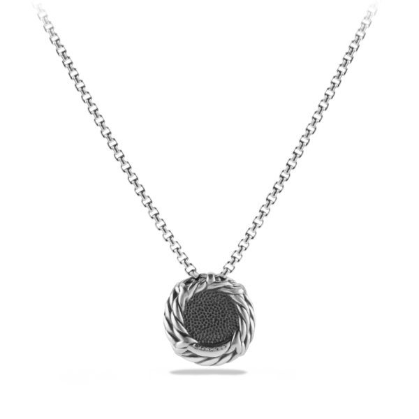 A close-up view of a silver pendant necklace with a circular, textured centerpiece. The pendant is suspended on a simple, box chain, featuring an intricate, twisted rope design around the edge of the circle. The background is white.