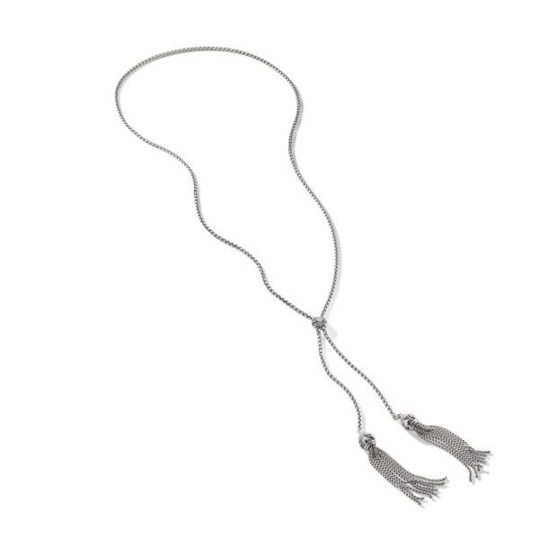 A silver lariat necklace with a delicate, thin chain that loops together in the center, leading to two tassels at the ends. Each tassel consists of multiple silver strands, creating a fringe effect. The necklace has a simple, elegant design.