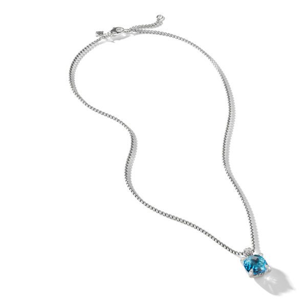 A delicate silver chain necklace with a single blue gemstone pendant. The pendant, shaped like a teardrop, is set in a simple metal clasp. The chain has an adjustable clasp at the end. The necklace rests on a white background, casting a faint shadow.