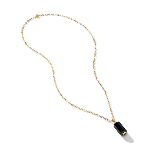 A delicate gold chain necklace features a small, rectangular black pendant with a cylindrical shape hanging from it. The pendant appears to be made of a shiny, opaque material, creating a sophisticated and elegant look. The chain forms a loose, looped arrangement.