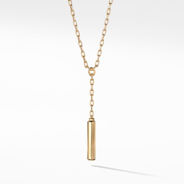 A gold lariat necklace featuring a sleek, cylindrical pendant hanging vertically from a delicate gold chain. The chain has an interlocking pattern and the pendant dangles at the center. The background is a plain white, making the gold necklace stand out vividly.