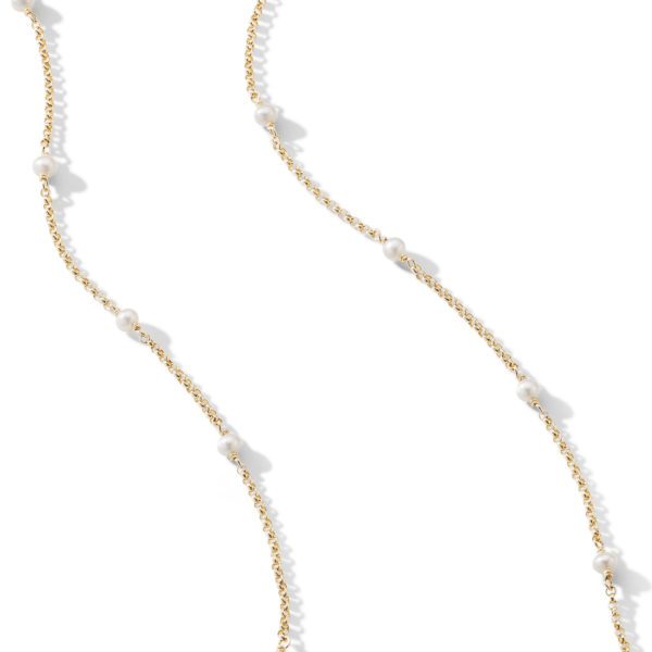 A delicate, gold chain necklace with evenly spaced, small white pearls. The necklace is arranged in a wavy pattern against a white background.