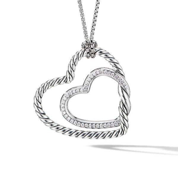 A silver necklace features two intertwined heart-shaped pendants. One heart has a twisted rope design, while the other is adorned with small sparkling stones. The pendants hang from a fine silver chain and cast a shadow on a white background.