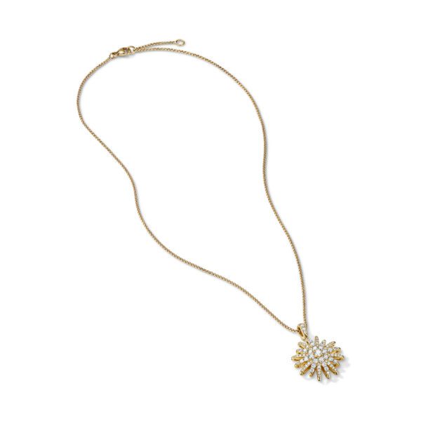 A delicate gold necklace with a radiant, sunburst-shaped pendant adorned with small clear gemstones. The pendant has a detailed, intricate design, and the necklace is laid flat on a plain white background.