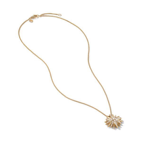 A gold necklace with a delicate chain features a pendant shaped like a sunburst adorned with small crystals, laid on a white background.