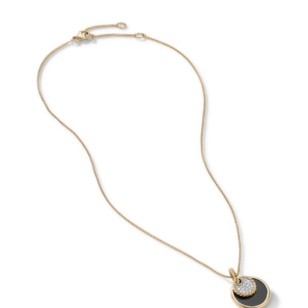 A gold necklace with a thin chain featuring a pendant with two overlapping circular elements. One element is black, and the other is encrusted with small, sparkling crystals. The necklace is unclasped and arranged in a curved shape.