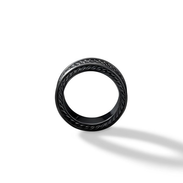 A black ring with intricate, braided detailing on its outer surface is shown on a white background. The ring casts a soft shadow to the right, emphasizing its circular shape and texture.