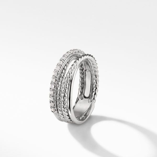 A silver ring featuring multiple intertwined bands, some plain and others adorned with small clear gemstones, creating a twisted, braided design. The ring casts a soft shadow on the white surface below.