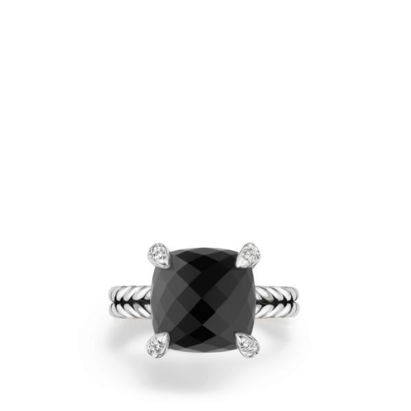 A silver ring featuring a large, cushion-cut black gemstone set in a four-prong setting. The prongs are adorned with small diamond accents, and the band has a twisted rope design.