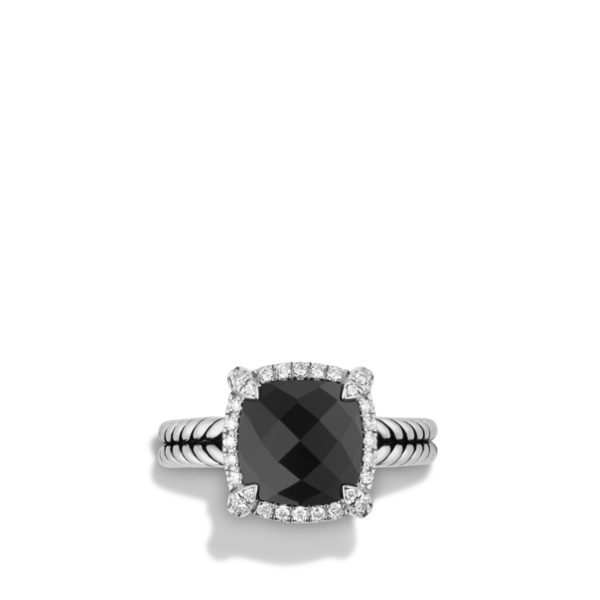 A silver ring with a large, cushion-cut black gemstone surrounded by small round diamonds. The band features a coiled design, giving it a textured appearance. The ring is set against a white background with shadows at the base.