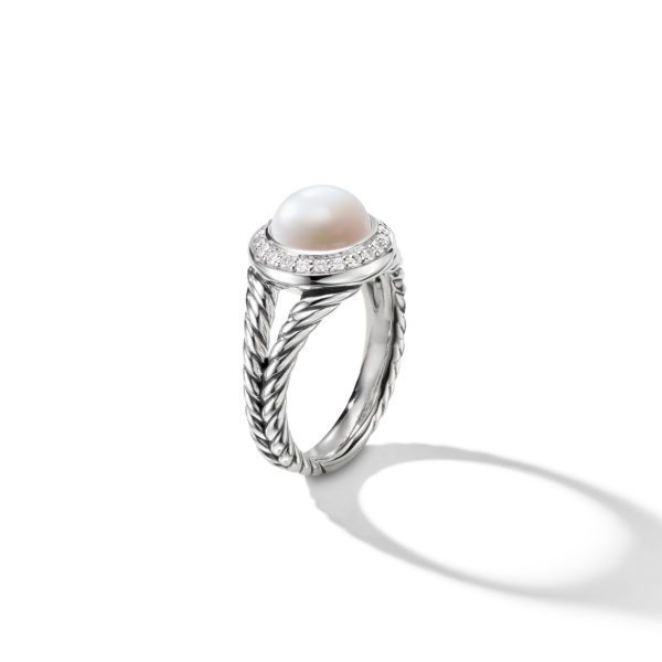 A silver ring with a textured band features a prominent white pearl set in the center, encircled by a ring of small, sparkling diamonds. The ring casts a soft shadow on the white surface beneath it.