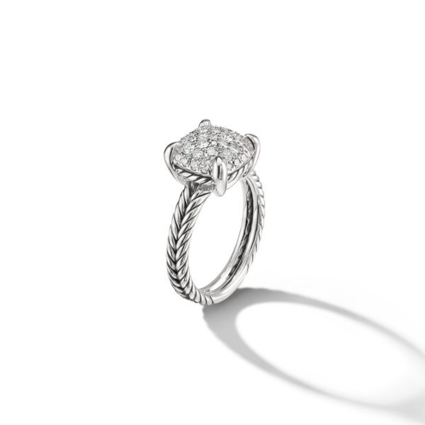 A silver ring with an intricate twisted band design is shown against a white background. The ring features a rectangular head adorned with multiple small sparkling diamonds, arranged closely together to create a glittering surface. A shadow of the ring is cast below.