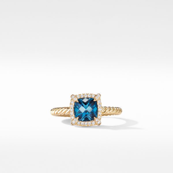 A gold ring with a twisted band features a square-cut blue gemstone, surrounded by a halo of small, sparkling diamonds on a white background. The ring is positioned upright, casting a slight shadow underneath.