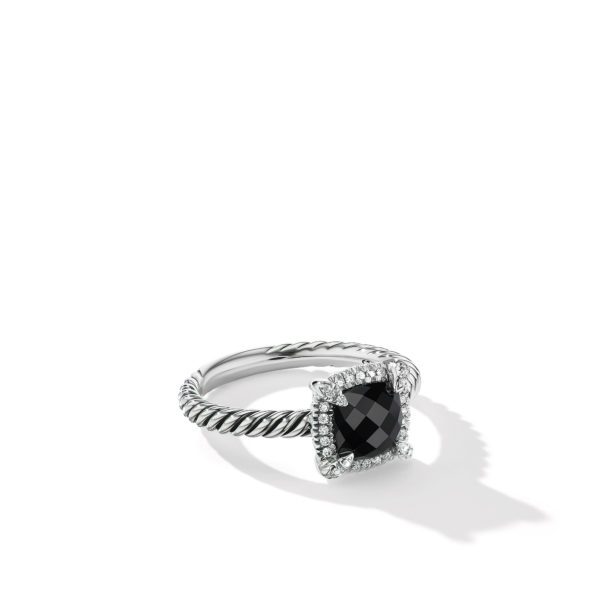 A close-up of a silver ring featuring a large square-cut black gemstone surrounded by small white diamonds. The band has a twisted rope design, and the ring is placed against a plain white background, casting a subtle shadow.