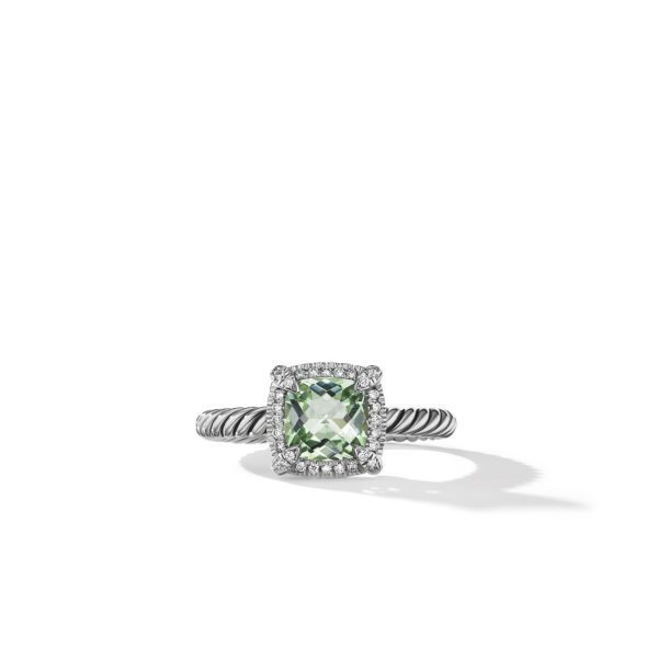 A ring featuring a twisted silver band and a cushion-cut green gemstone surrounded by small clear diamonds, resting on a white surface with a shadow.